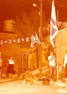 אייר תשל"ח 1978. טקס יום הזיכרון הראשון באלקנה. אודי הופנברג מוריד את הדגל לחצי התורן ושושי שור מחצרצת (למדה לחצרץ בתזמורת בית הספר ברמת גן). צילם: עקיבא איזנברג [באדיבות רחל ועקיבא איזנברג, תשפ"ה 2025]